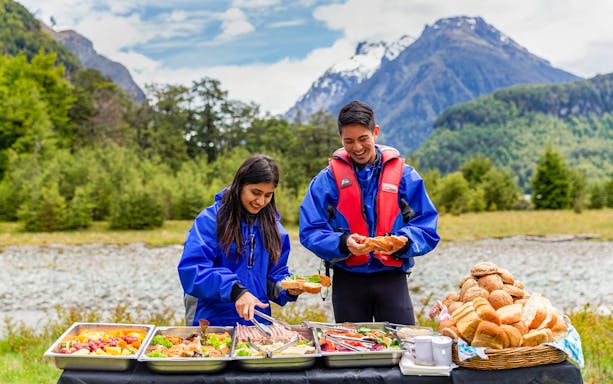 People enjoying a picnic with food trays in Dart River Funyaks, New Zealand.