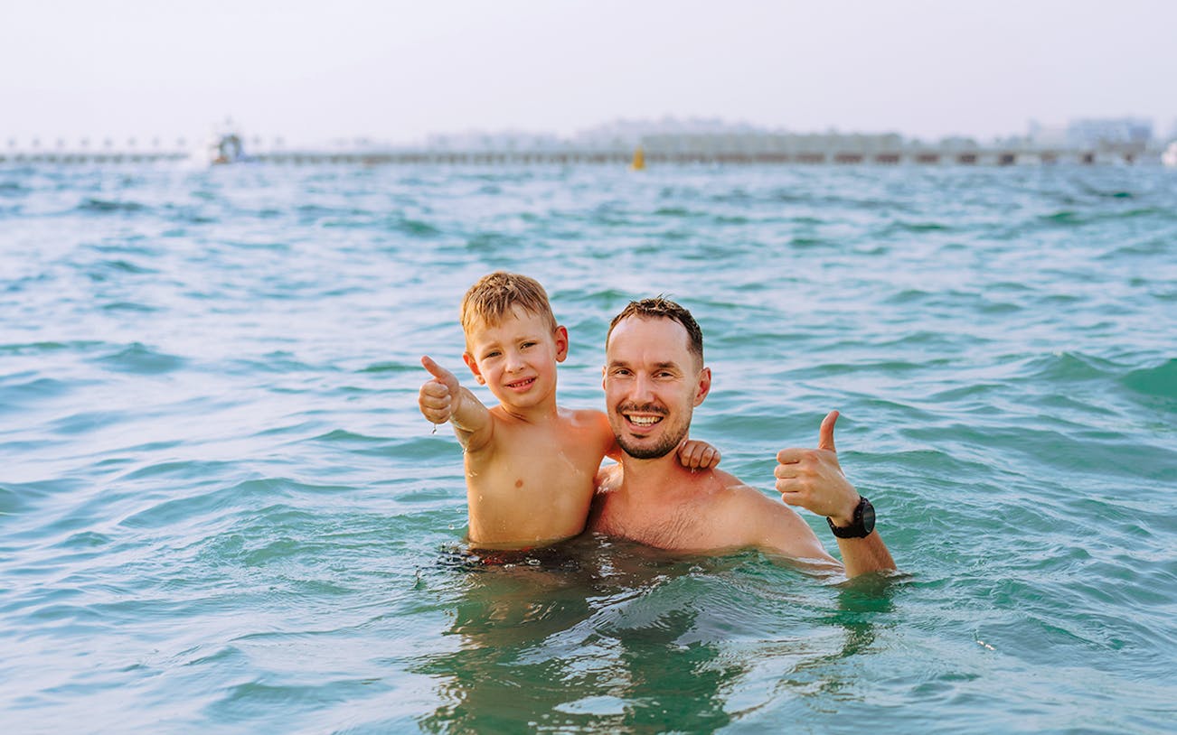 Father and son enjoying Jumeirah swimming tour in clear blue water.