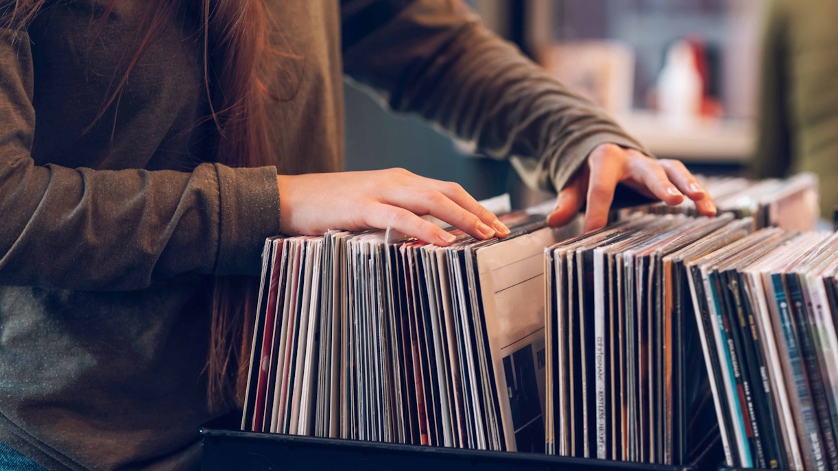 Person browsing vinyl records in a collection of rockstar artifacts.