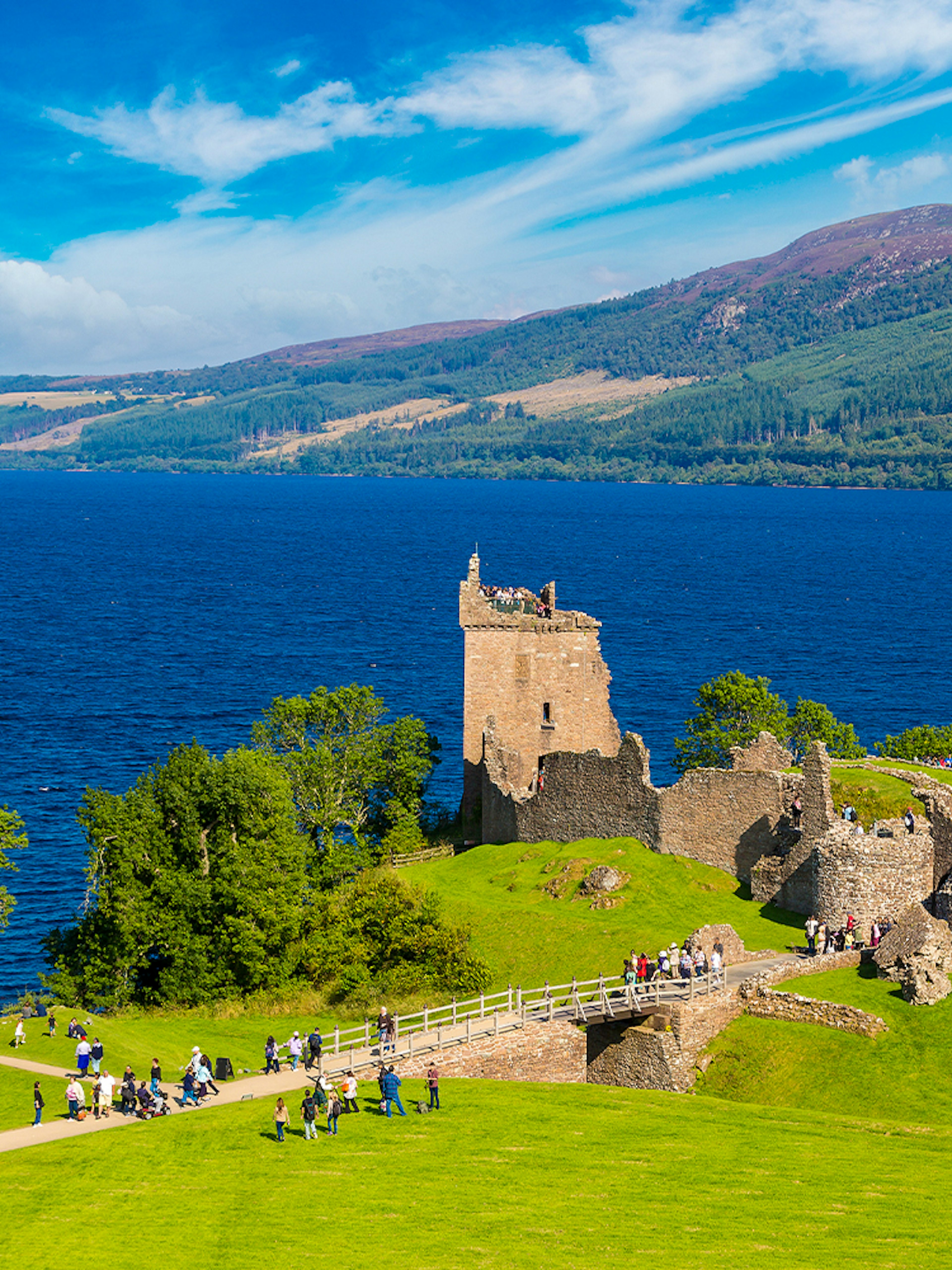 Urquhart Castle ruins overlooking Loch Ness in Scotland with visitors exploring the grounds.