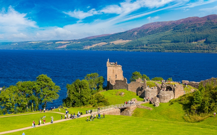 Urquhart Castle ruins overlooking Loch Ness in Scotland with visitors exploring the grounds.