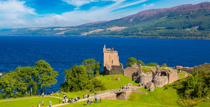 Urquhart Castle ruins overlooking Loch Ness in Scotland with visitors exploring the grounds.