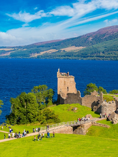 Urquhart Castle ruins overlooking Loch Ness in Scotland with visitors exploring the grounds.