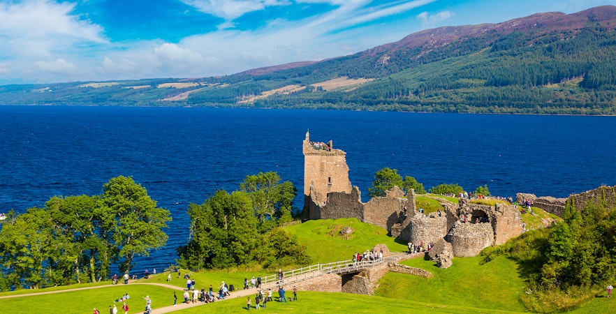 Urquhart Castle ruins overlooking Loch Ness in Scotland with visitors exploring the grounds.