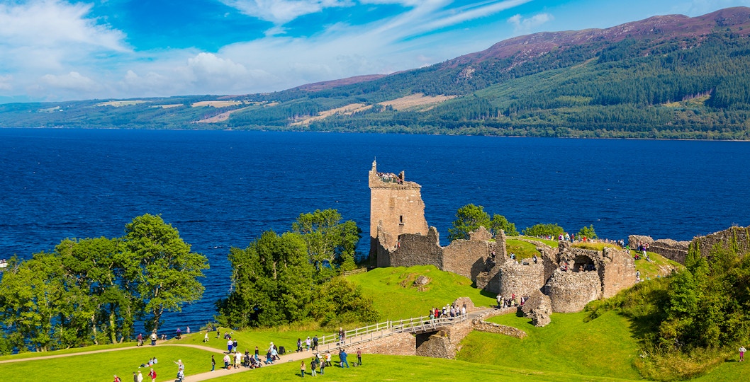 Urquhart Castle ruins overlooking Loch Ness in Scotland with visitors exploring the grounds.