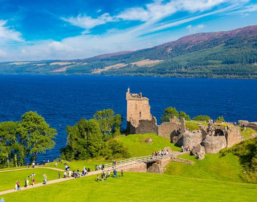 Urquhart Castle ruins overlooking Loch Ness in Scotland with visitors exploring the grounds.