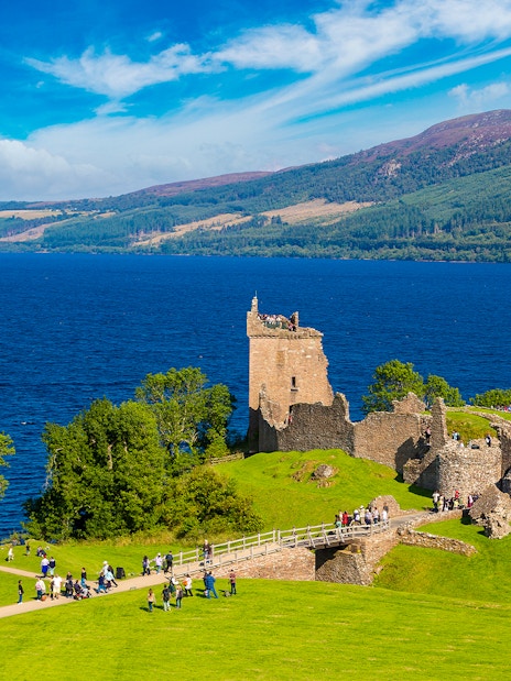 Urquhart Castle ruins overlooking Loch Ness in Scotland with visitors exploring the grounds.