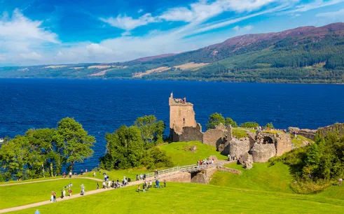 Urquhart Castle ruins overlooking Loch Ness in Scotland with visitors exploring the grounds.