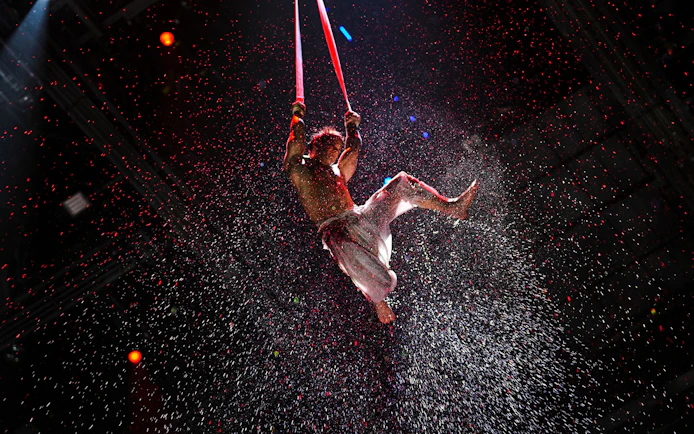 Aerial performer suspended in water spray during House of Dancing Water show.