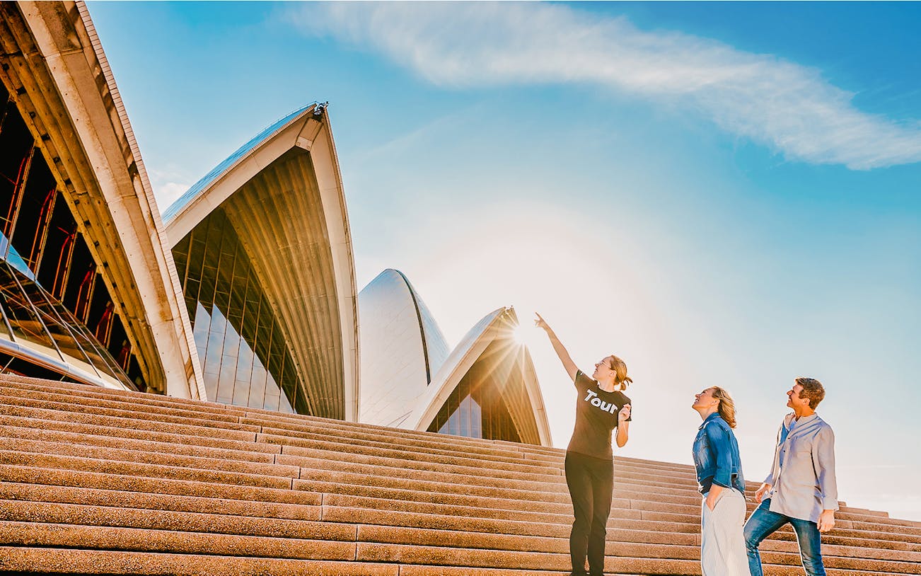 Tour guide pointing at Sydney Opera House sails with two tourists.