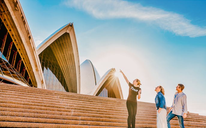 Tour guide pointing at Sydney Opera House sails with two tourists.