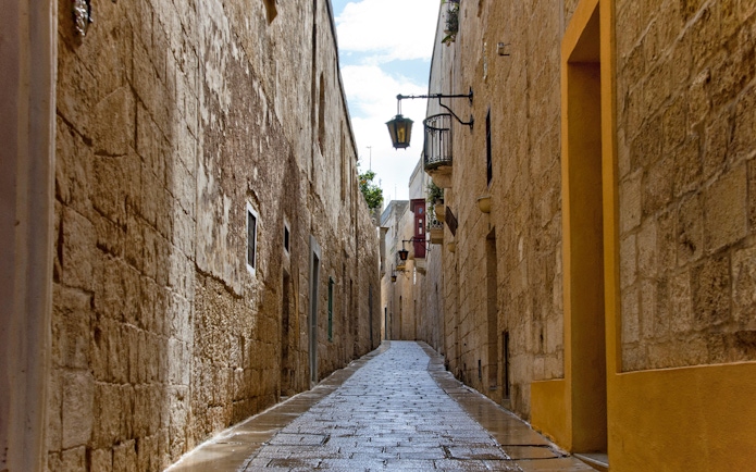 Narrow cobblestone street in Mdina, Malta, lined with historic stone buildings.