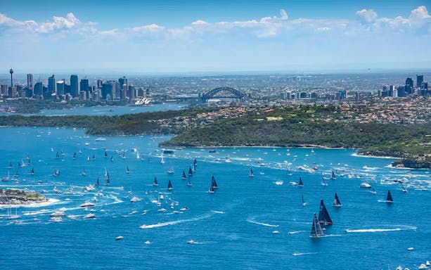 Sailboats racing in Sydney Harbour with city skyline and Sydney Harbour Bridge in the background.