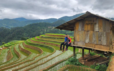 Couple sitting by a wooden hut overlooking rice terraces in Mu Cang Chai, Vietnam.