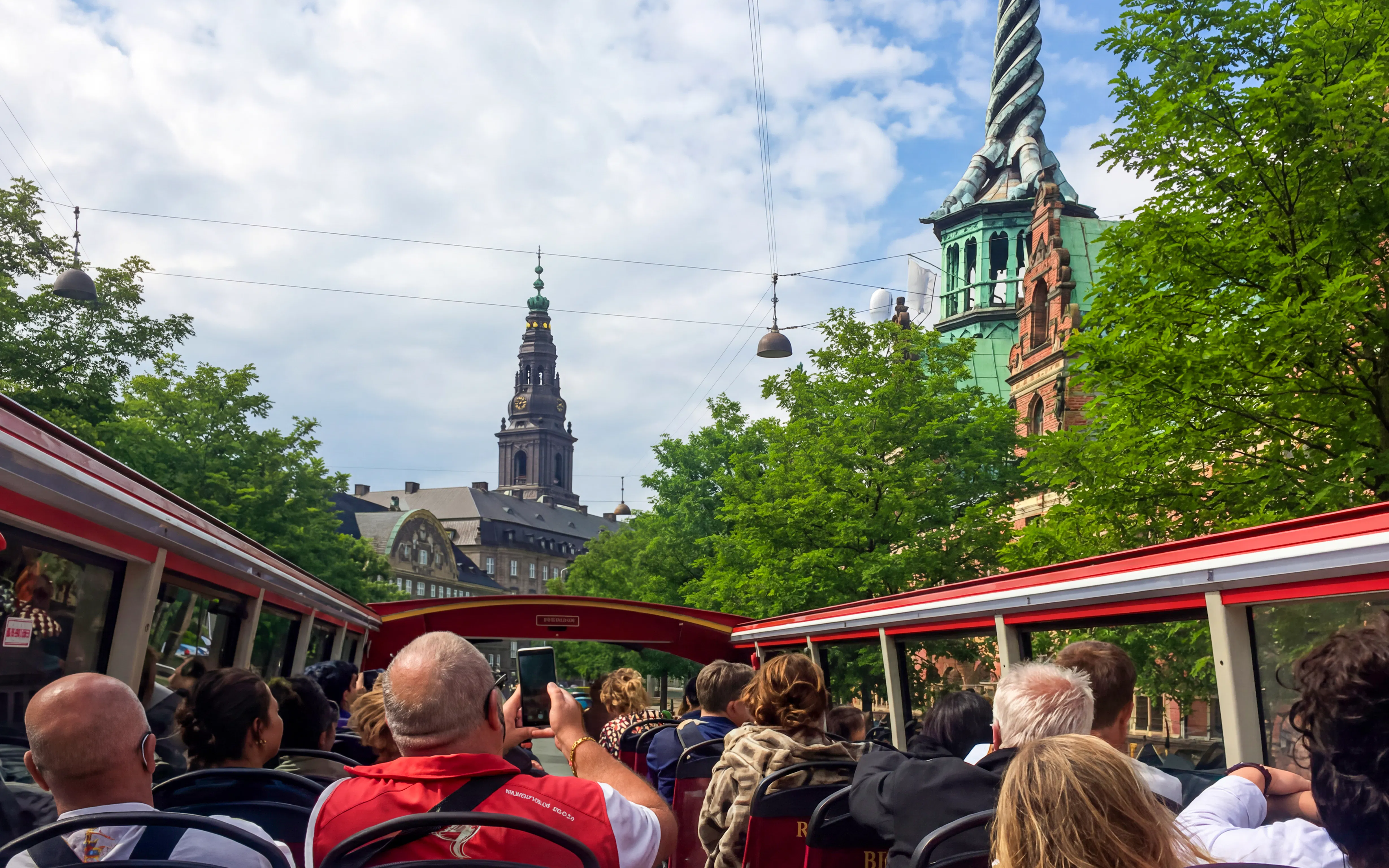 Copenhagen tourists on hop-on hop-off bus with view of city architecture and spire.