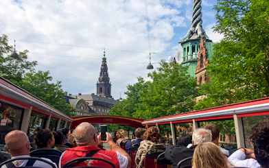 Copenhagen tourists on hop-on hop-off bus with view of city architecture and spire.