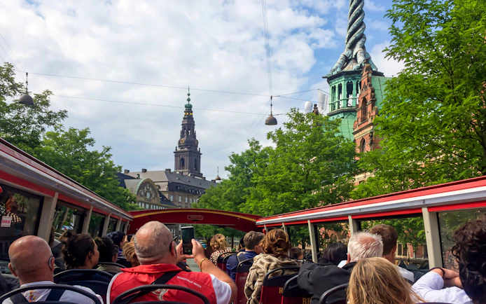 Copenhagen tourists on hop-on hop-off bus with view of city architecture and spire.