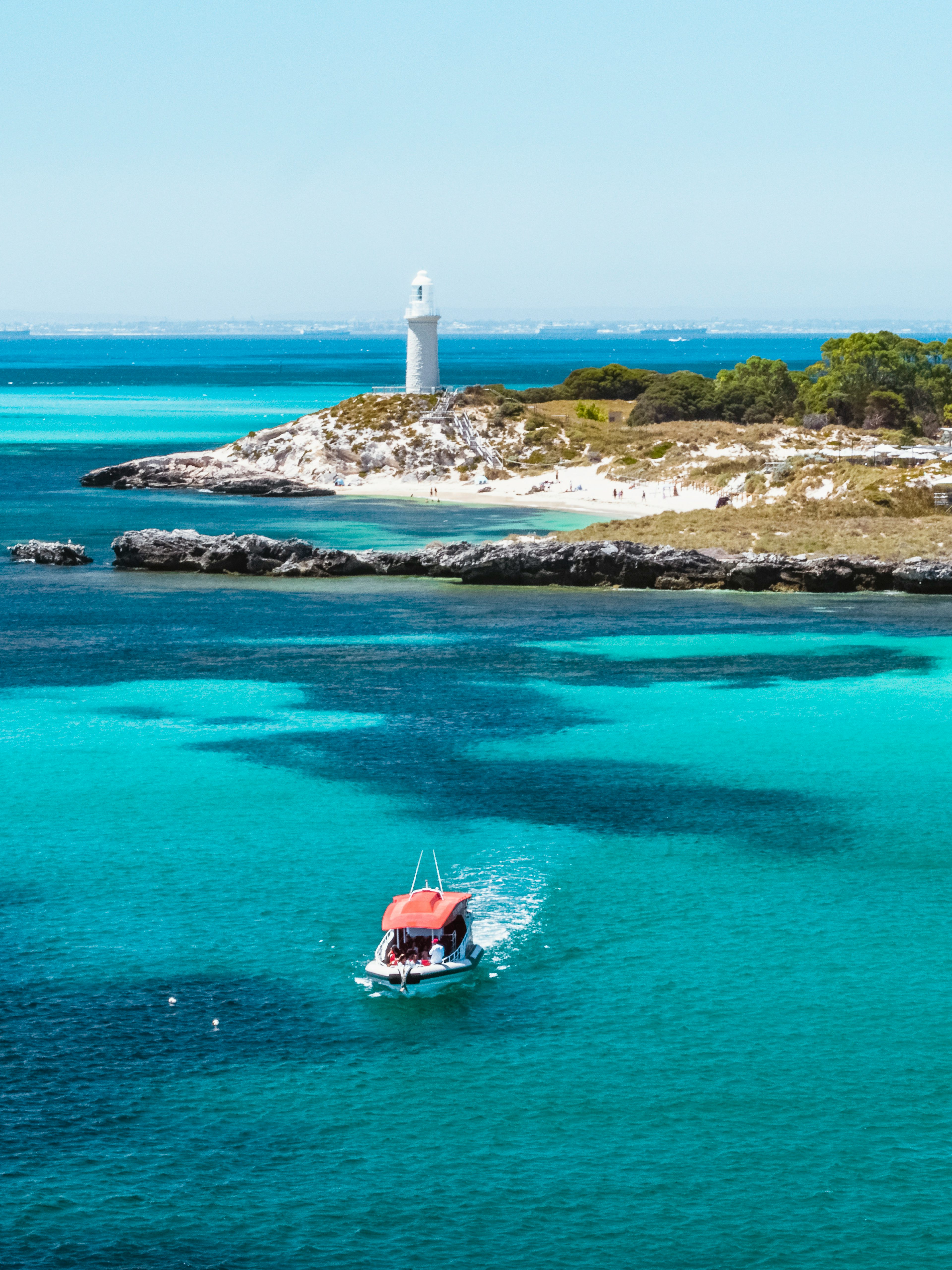 Small red boat in turquoise water near a lighthouse and island.