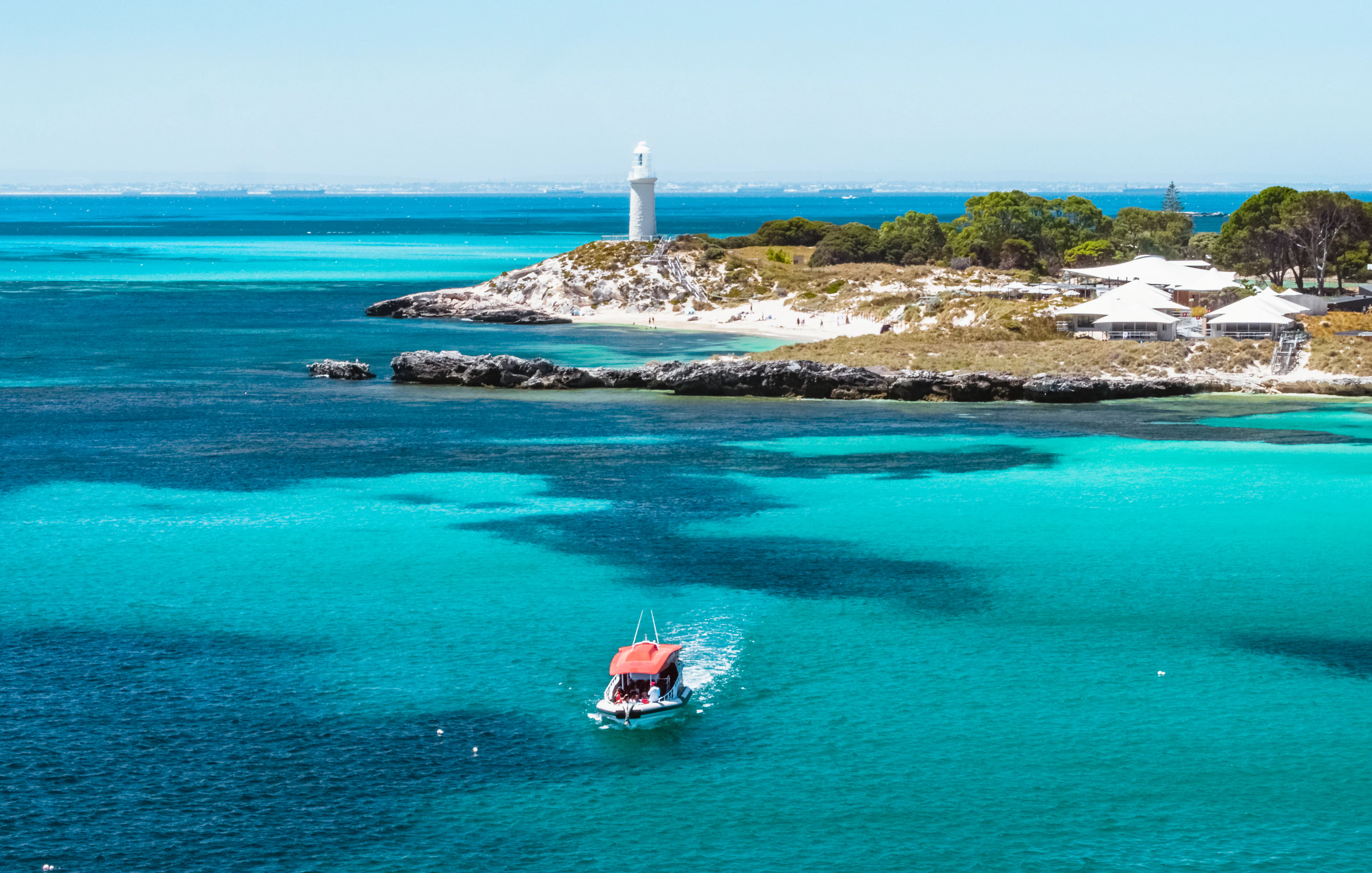 Small red boat in turquoise water near a lighthouse and island.