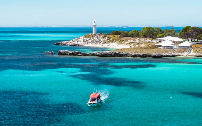 Small red boat in turquoise water near a lighthouse and island.