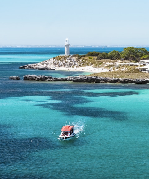 Small red boat in turquoise water near a lighthouse and island.
