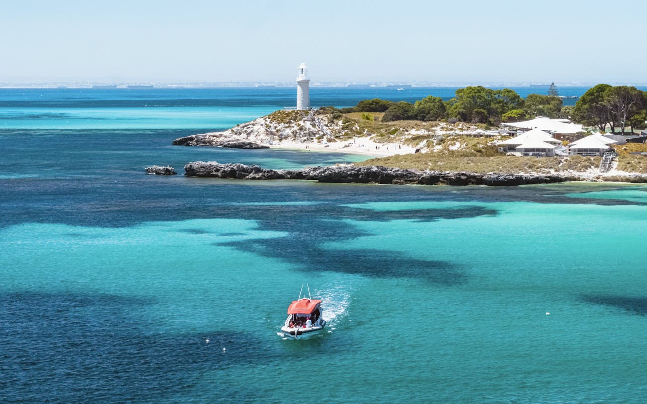 Small red boat in turquoise water near a lighthouse and island.