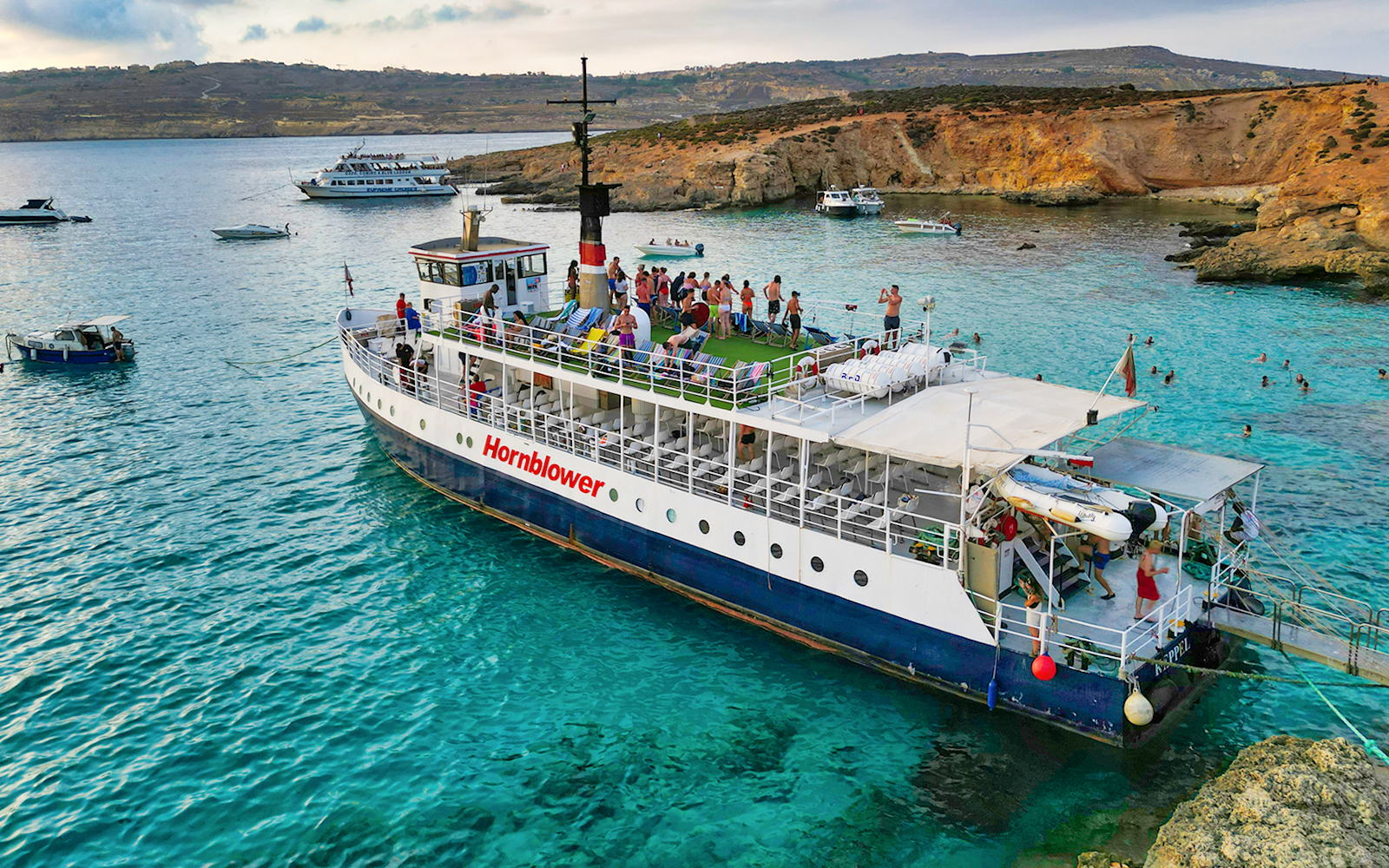Cruise ship at Blue Lagoon with tourists enjoying the view and swimming in clear waters.