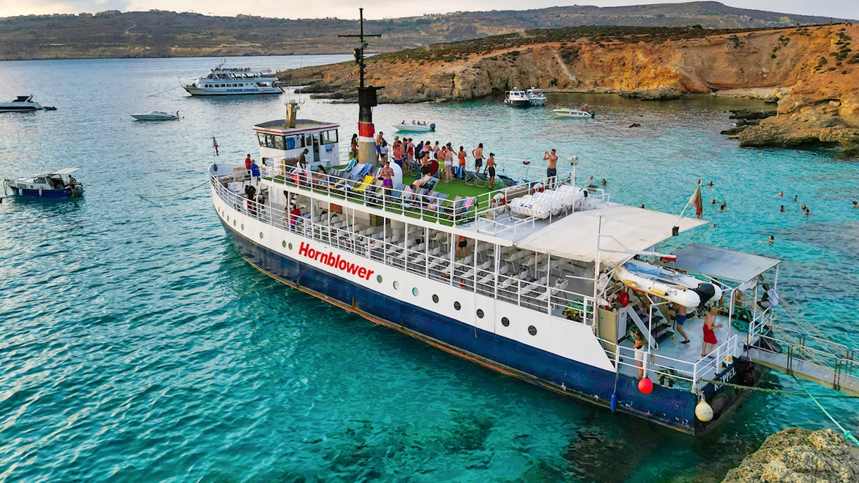 Boat cruising through Blue Lagoon's turquoise waters, surrounded by rocky cliffs, Malta.
