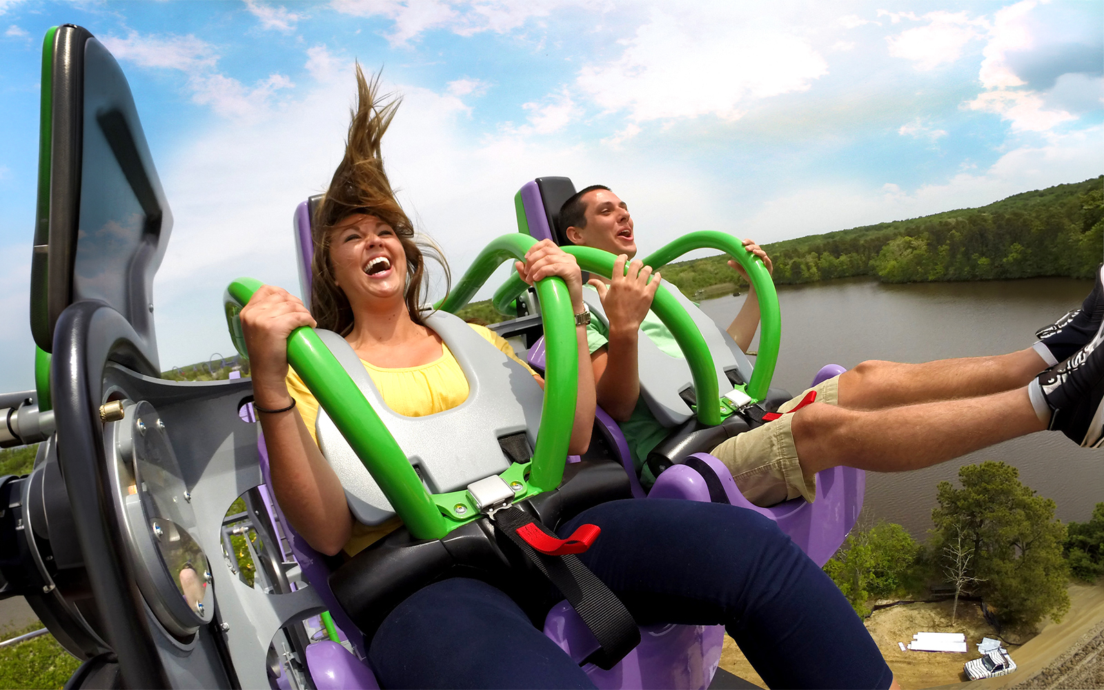 Riders enjoying THE JOKER™ roller coaster at Six Flags Great Adventure with a lake view.