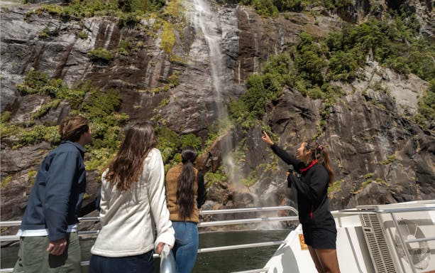 Tourists on a Milford Sound cruise observing a waterfall cascading down a rocky cliff.