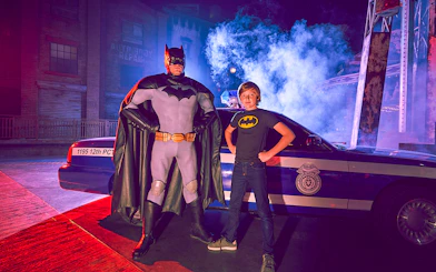 Superhero and child pose by police car at Yas Island park.