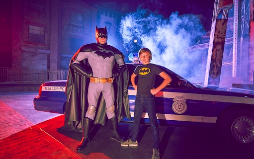 Superhero and child pose by police car at Yas Island park.