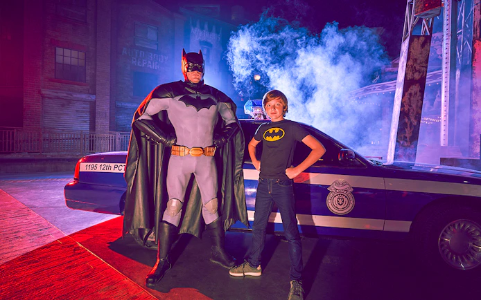 Superhero and child pose by police car at Yas Island park.