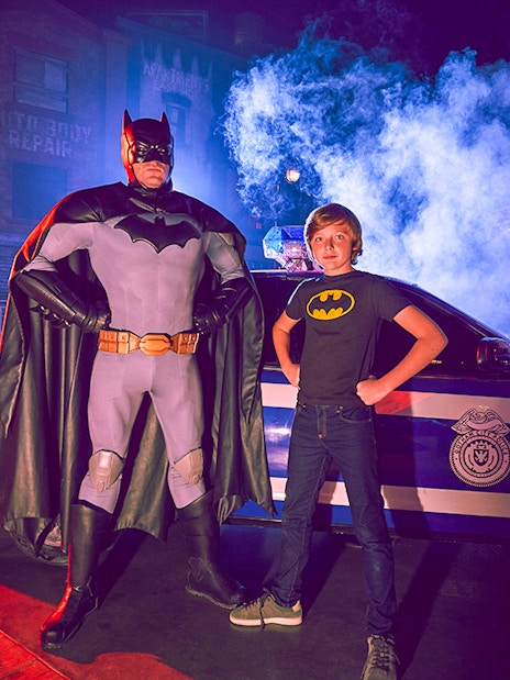 Superhero and child pose by police car at Yas Island park.
