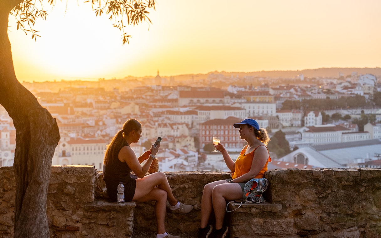 Visitors enjoying wine on St. George’s Castle terrace at sunset, Lisbon.