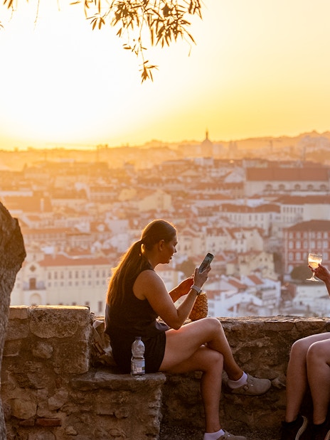 Visitors enjoying wine on St. George’s Castle terrace at sunset, Lisbon.