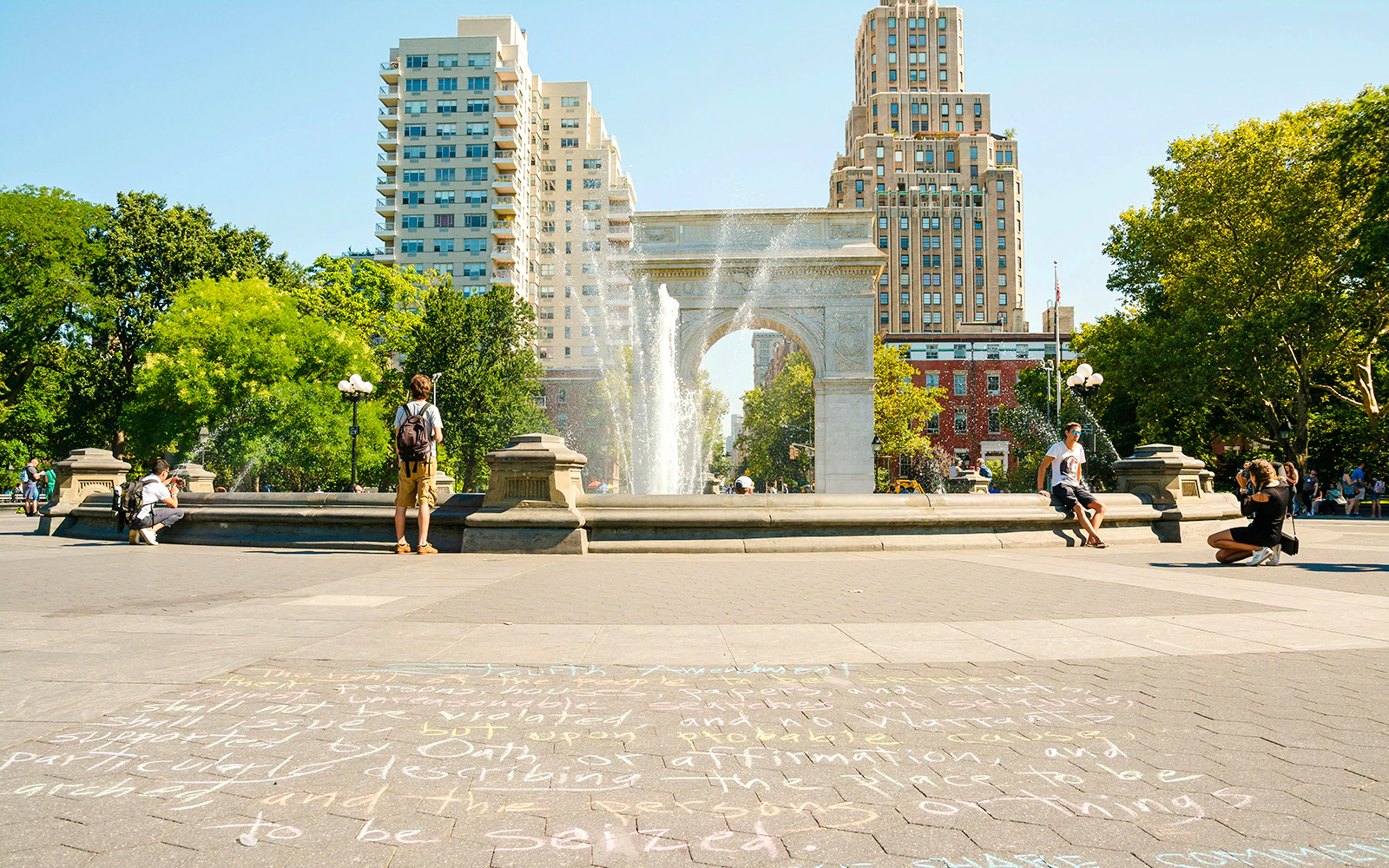 Washington Square Park fountain and arch with people enjoying a sunny day in NYC.