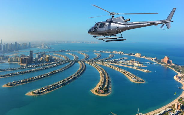 Helicopter flying over Dubai's Palm Jumeirah with city skyline in view.
