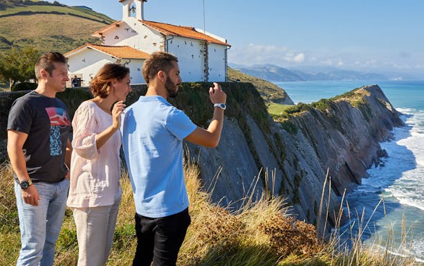 Tourists enjoying coastal views near a chapel on a guided tour from San Sebastian to Zarautz, Getaria, and Zumaia.