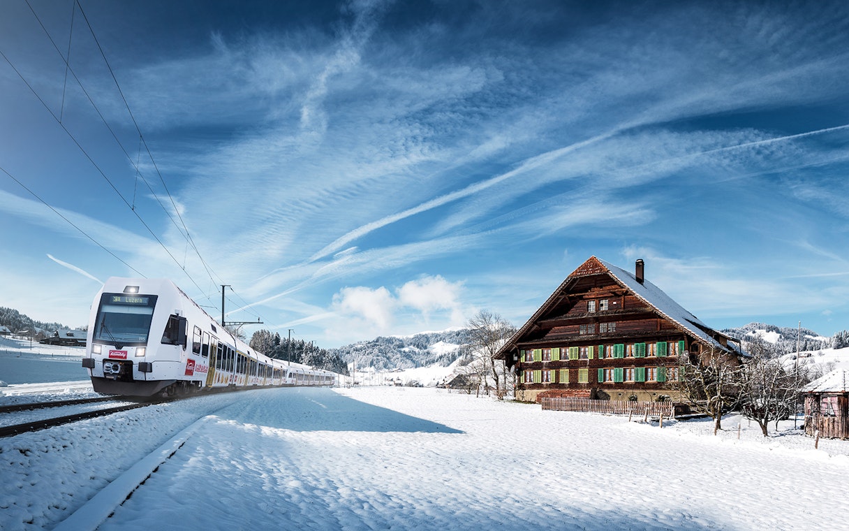 Train on Lucerne–Interlaken Express passing snowy Swiss countryside with traditional chalet.