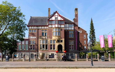 Exteriors of Moco Museum in Amsterdam with historic architecture and pink banners.