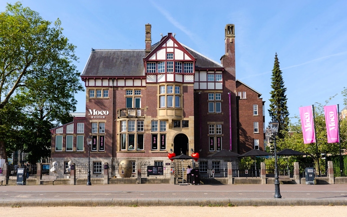 Exteriors of Moco Museum in Amsterdam with historic architecture and pink banners.