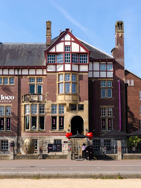 Exteriors of Moco Museum in Amsterdam with historic architecture and pink banners.