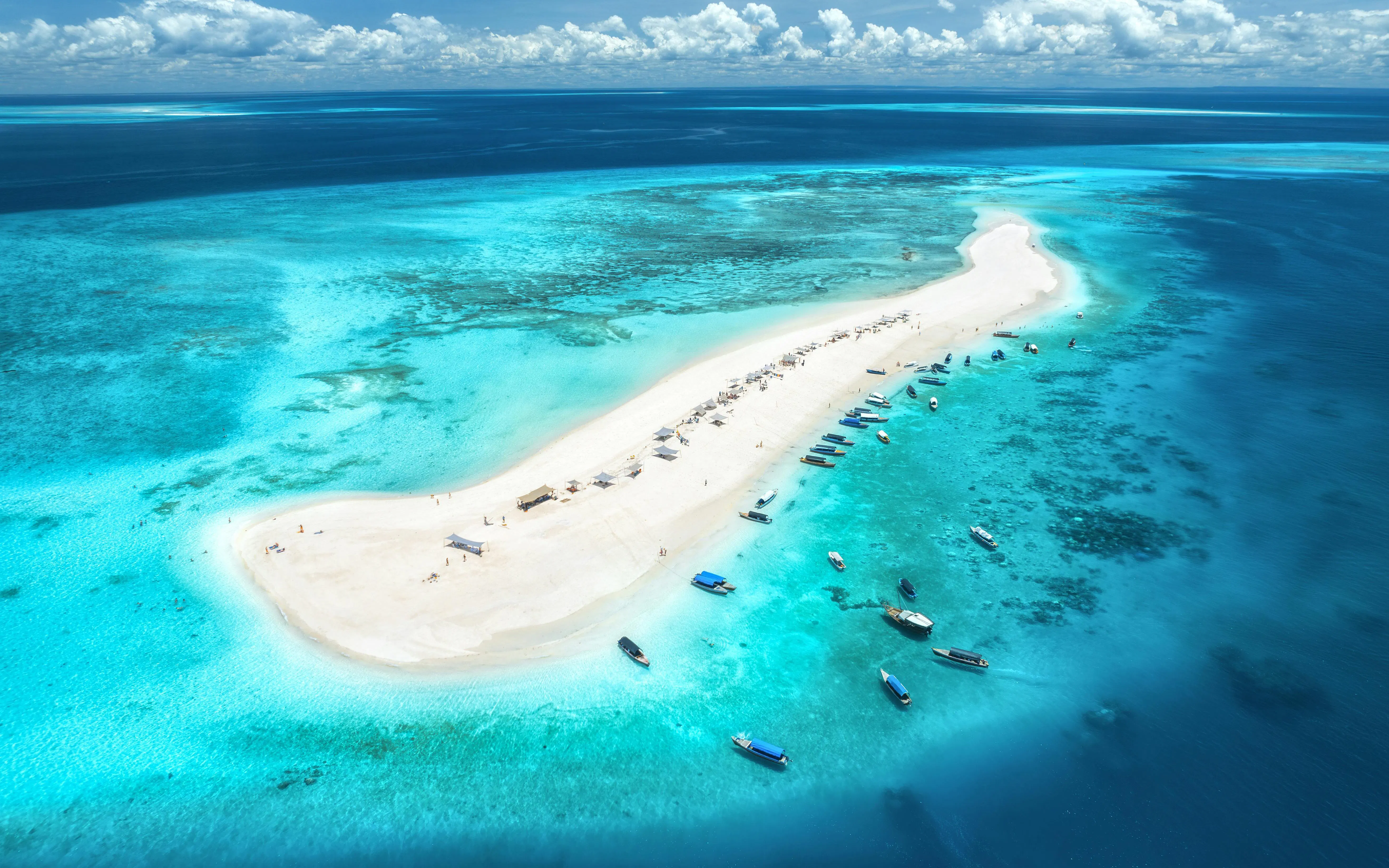 Aerial view of Nakupenda Island with boats along the sandy shore and turquoise waters.