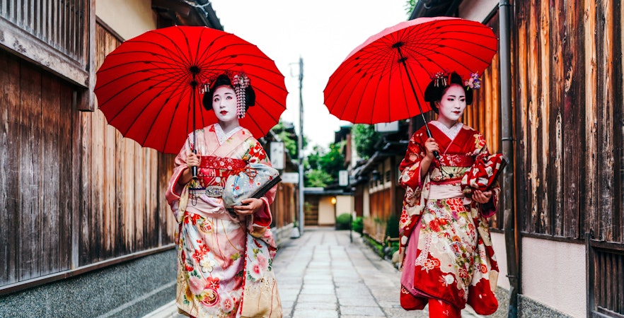 Maiko geisha walking with red umbrellas in Gion, Kyoto.