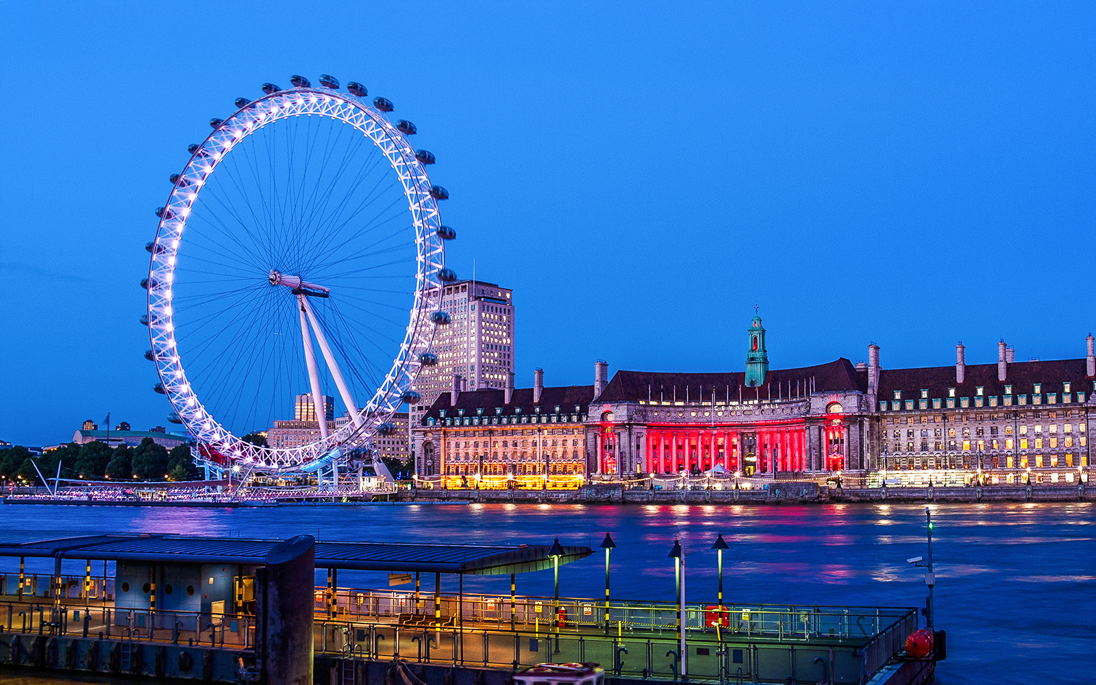 London Eye illuminated at night from the South Bank, with County Hall in the background.