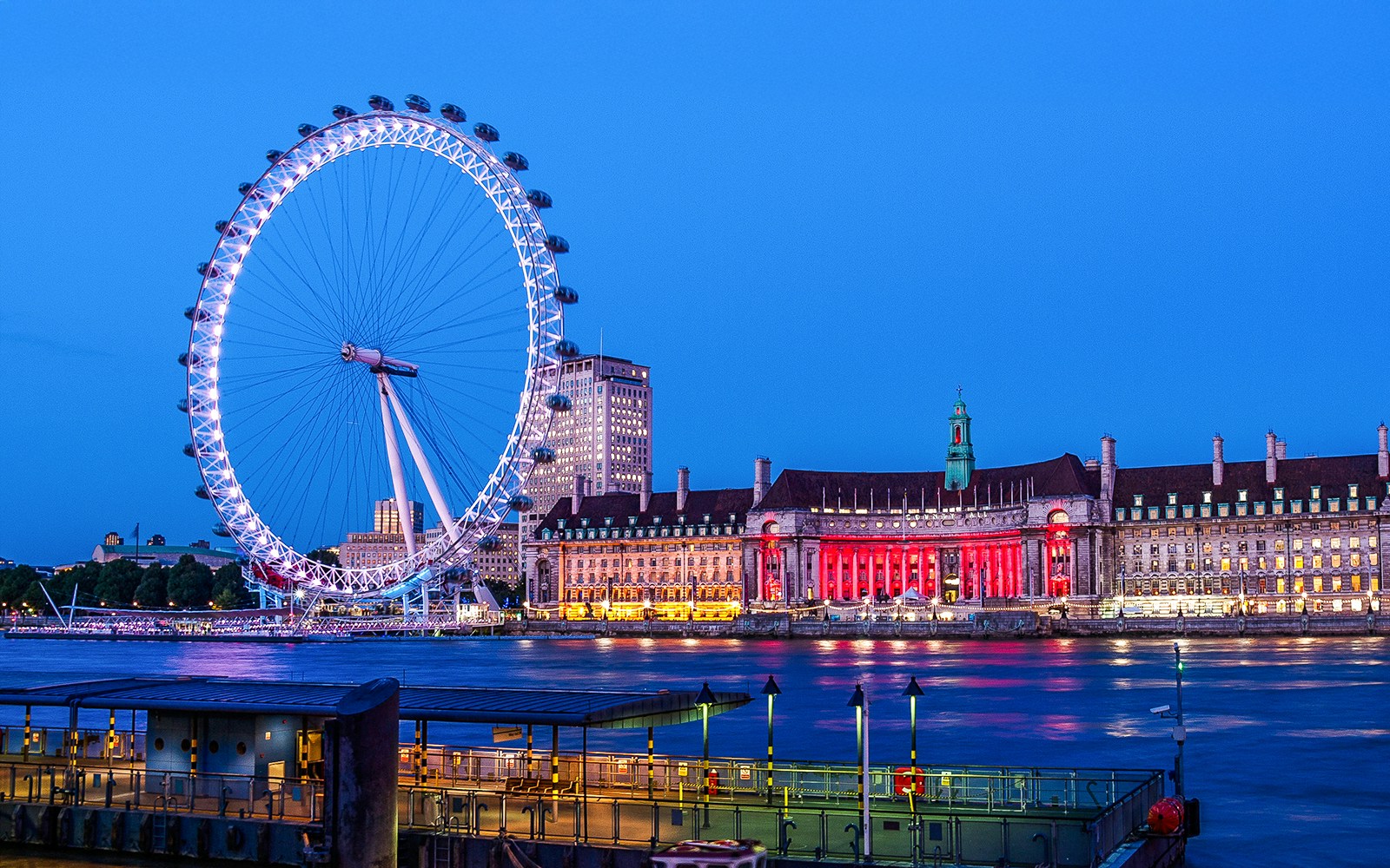 London Eye illuminated at night from the South Bank, with County Hall in the background.