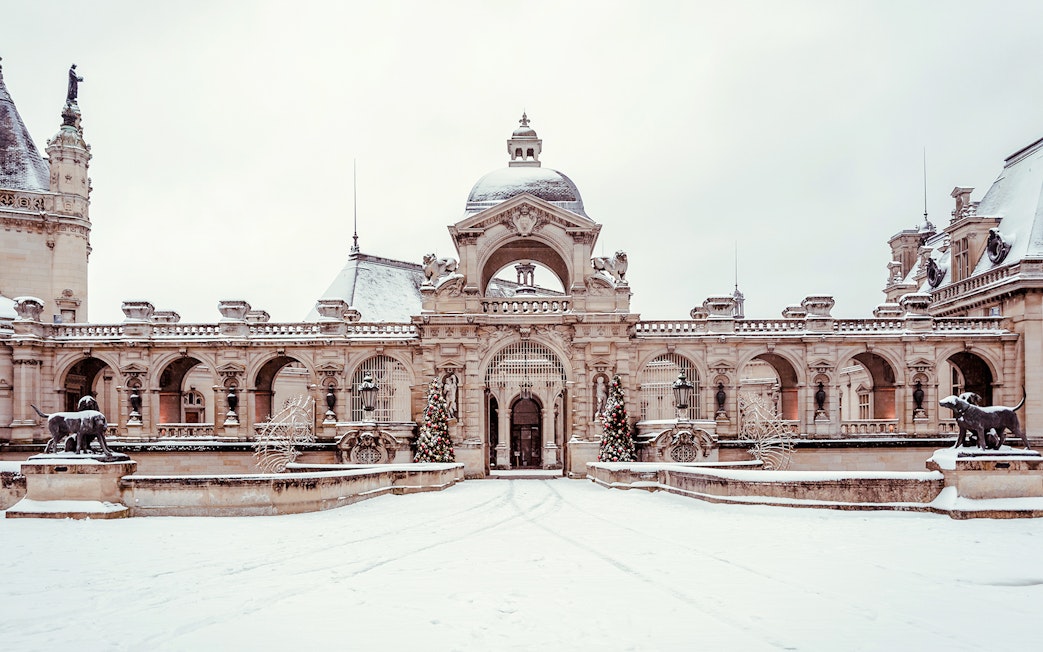 Chateau of Chantilly entrance with snow-covered courtyard and decorative statues.