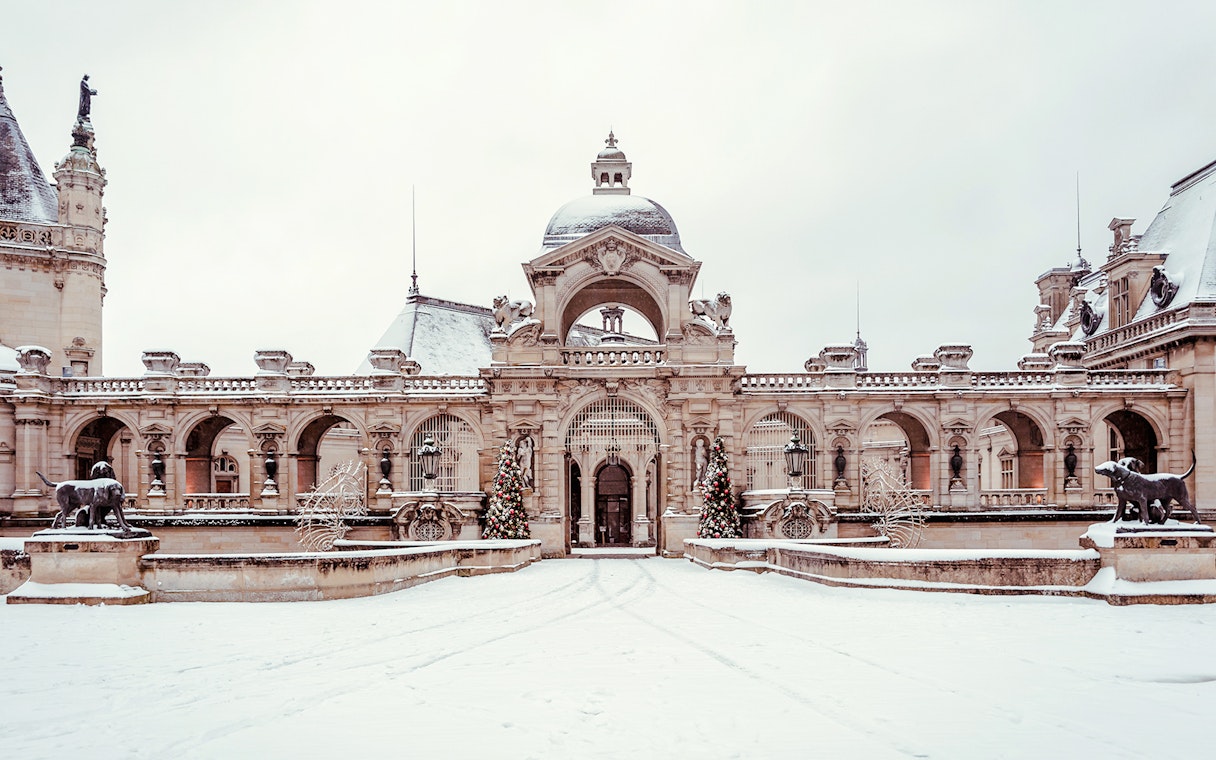 Chateau of Chantilly entrance with snow-covered courtyard and decorative statues.