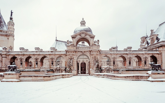 Chateau of Chantilly entrance with snow-covered courtyard and decorative statues.